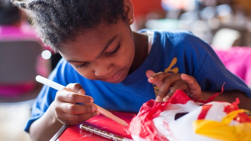 A child sat at a table with craft materials decorating a mask